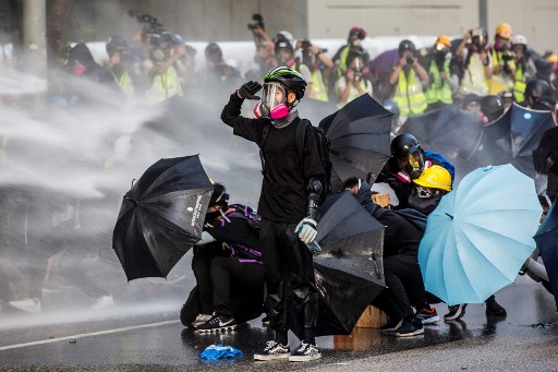 Pro-democracy protesters react as police fire water cannons outside the government headquarters in Hong Kong on September 15, 2019. – Hong Kong riot police fired tear gas and water cannons on September 15 at hardcore pro-democracy protesters hurling rocks and petrol bombs, in a return to the political chaos plaguing the city. (Photo by Isaac LAWRENCE / AFP)