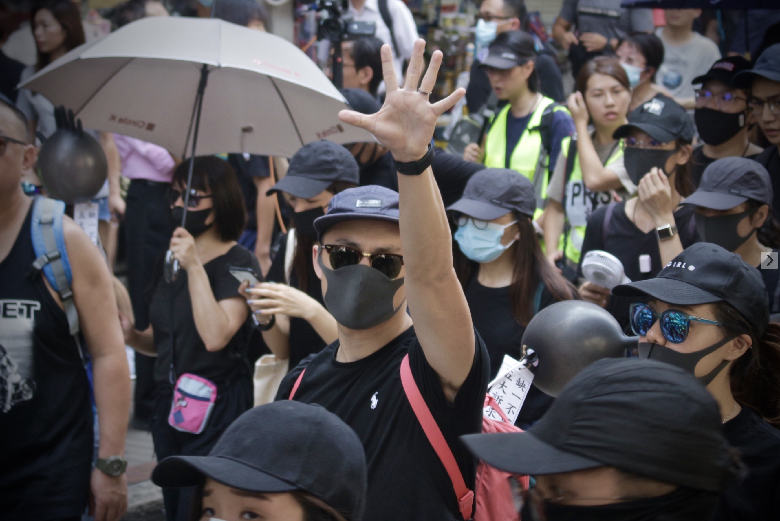 A masked protester holds up five fingers, the gesture used to represent the slogan ‘five demands, not one less.’ Photo by Vicky Wong.