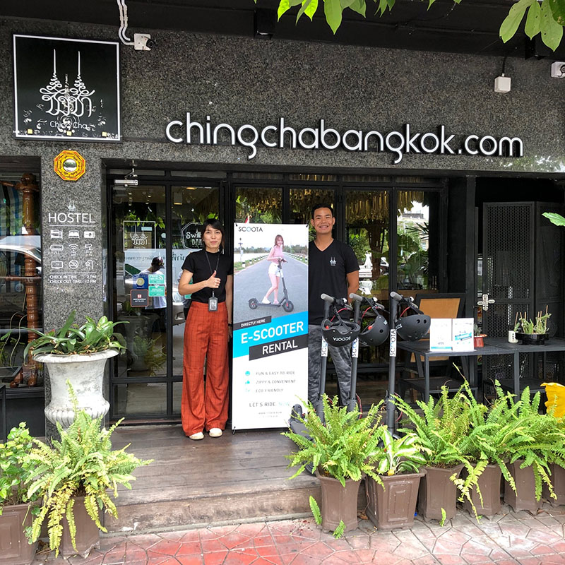 Pookun Trichomwaree, at left, pose with Scoota e-scooters in front of her Chingcha Bangkok Hostel. 