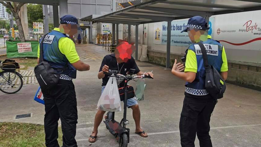 Land Transport Authority officers intercept an e-scooter rider traveling on a footpath in Sengkang. Faces and shopping bag blurred by the authority. Photo: LTA/Facebook