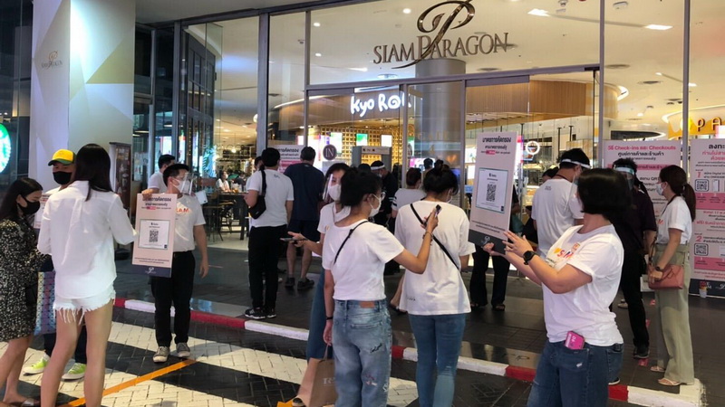 People wait to scan a QR code to register their arrival Sunday at the entrance of the Siam Paragon shopping mall in Bangkok.