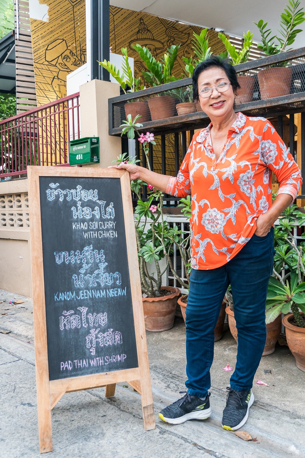 Siripha ‘Lek’ Chariton poses with a sign in front of her restaurant.