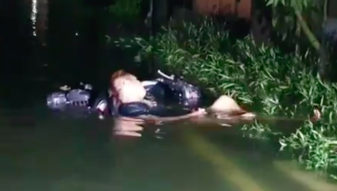 An allegedly intoxicated Jakarta man sleeping in floodwater with his motorcycle serving as a headrest. Photo: Video screengrab