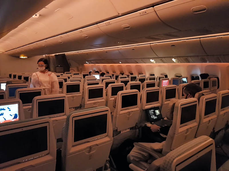 An Emirates flight attendant in full personal protective equipment walks down the aisle of a near-empty Boeing 777-300ER prior to landing in Dubai.