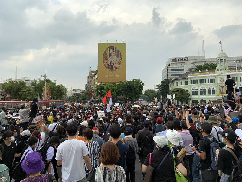 A large portrait of King Vajiralongkorn looms over protesters as they march along the royal avenue.