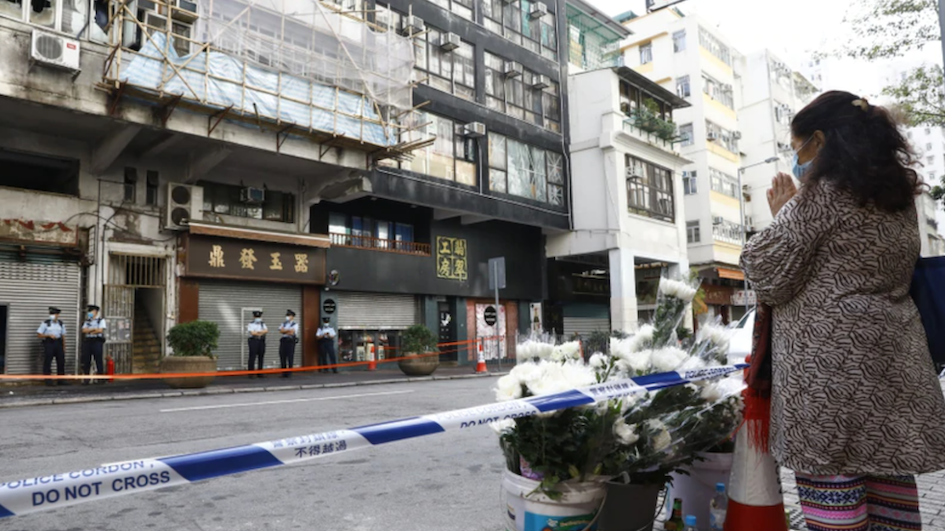 A woman leaves flowers opposite the building where the restaurant caught fire in Yau Ma Tei on Nov. 16, 2020. Photo via Apple Daily