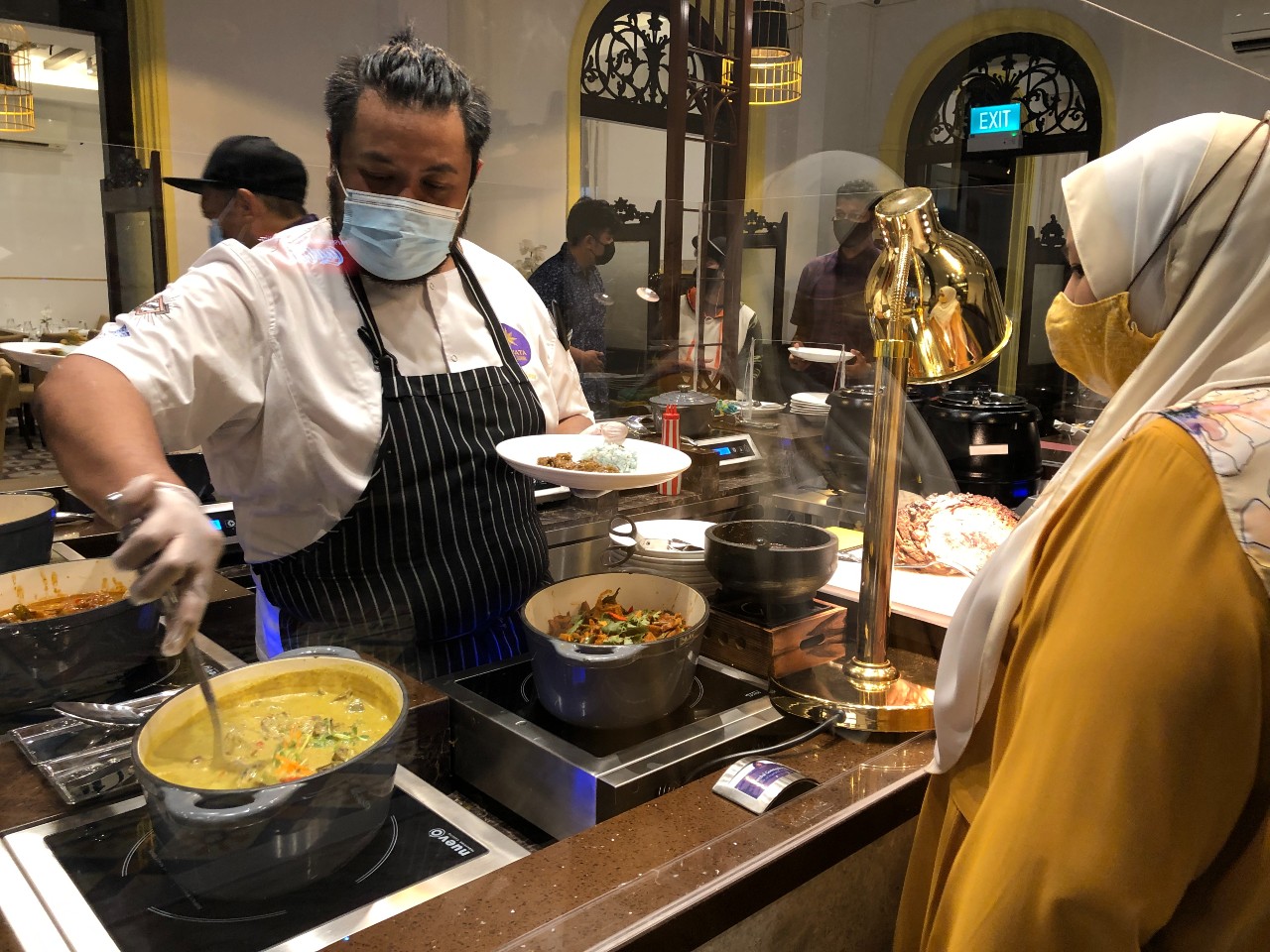 Executive chef Firdauz Nasir scooping out gravy while a diner looks from behind a plastic barrier. Photo: Coconuts 