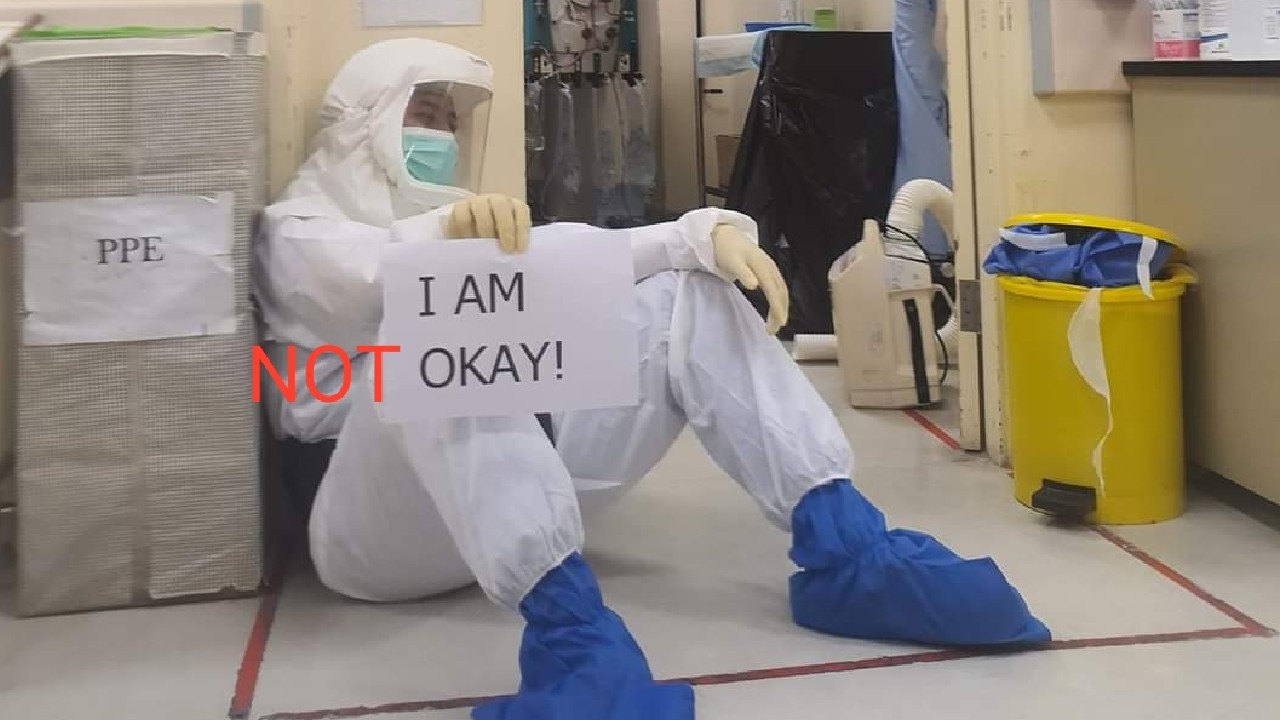 A health worker in PPE and holding up a sign that says “I AM OKAY!.” Edited photo: HartalDoktorKontrak/Twitter
