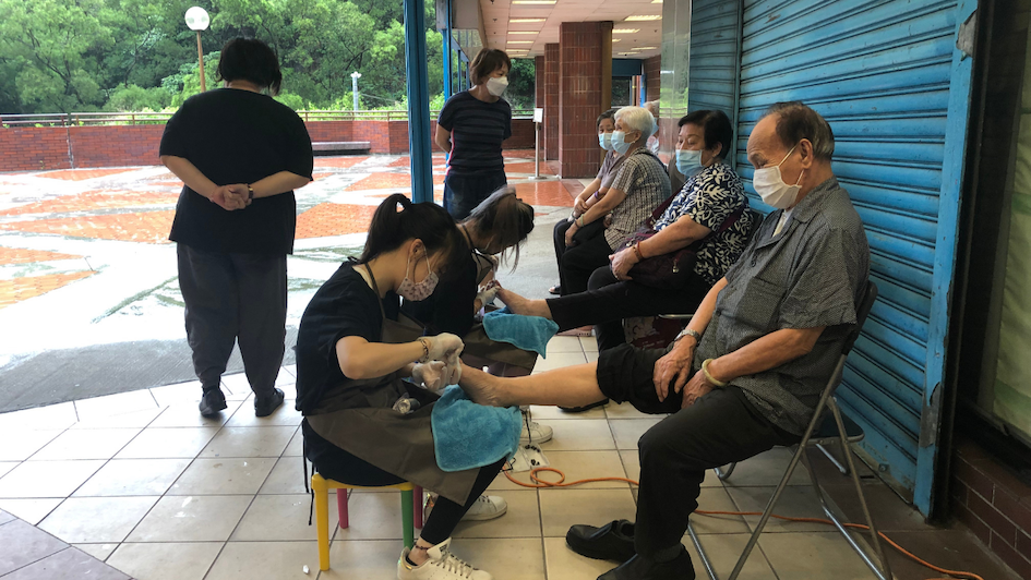 Cass Ng and a volunteer trim toenails for senior citizens at a neighborhood mall in Lei Tung. Photo: Coconuts Media