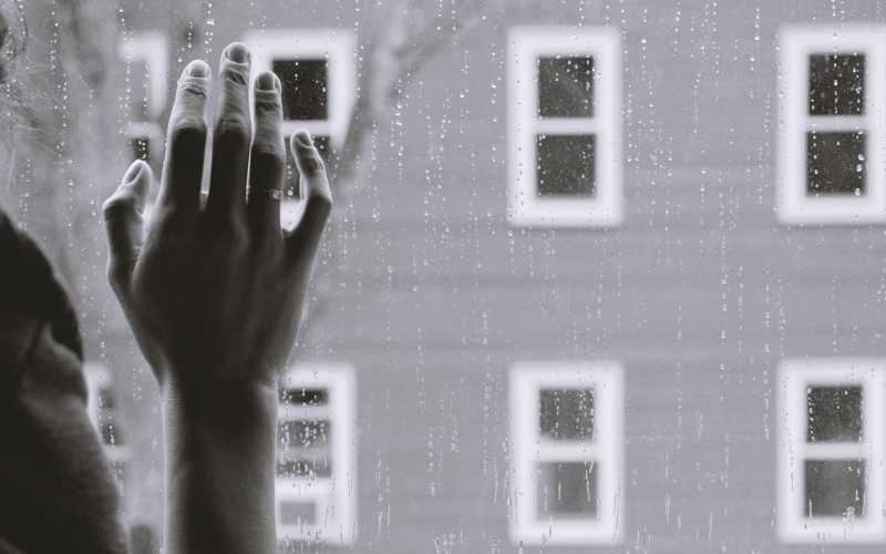 A person places their hand on a window on a rainy day. Photo: Kristina Tripkovic/Unsplash
