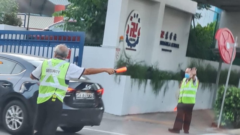 School security guard Neo Ah Whatt, at left, ushering cars into the Red Swastika School in Bedok this morning. Photo: SG Road Vigilante
