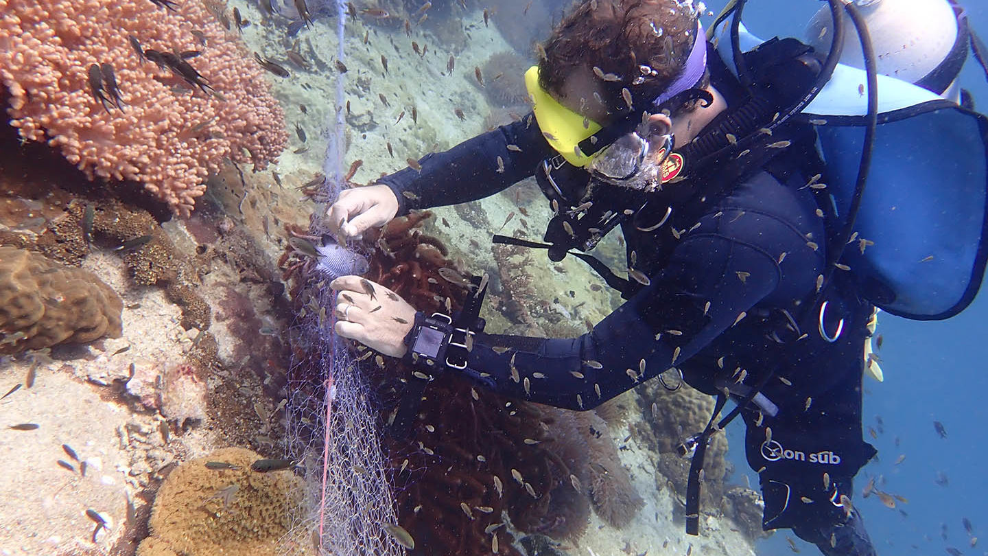 A diver painstakingly removes a discarded fishing net snagged across a coral reef. Photo: Thai Ocean Academy / Courtesy