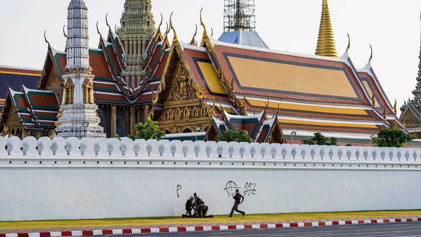 Police officers apprehend a man spraying graffiti Tuesday on a wall of the Grand Palace in Bangkok. Photo: Egg Cat Cheese / Facebook
